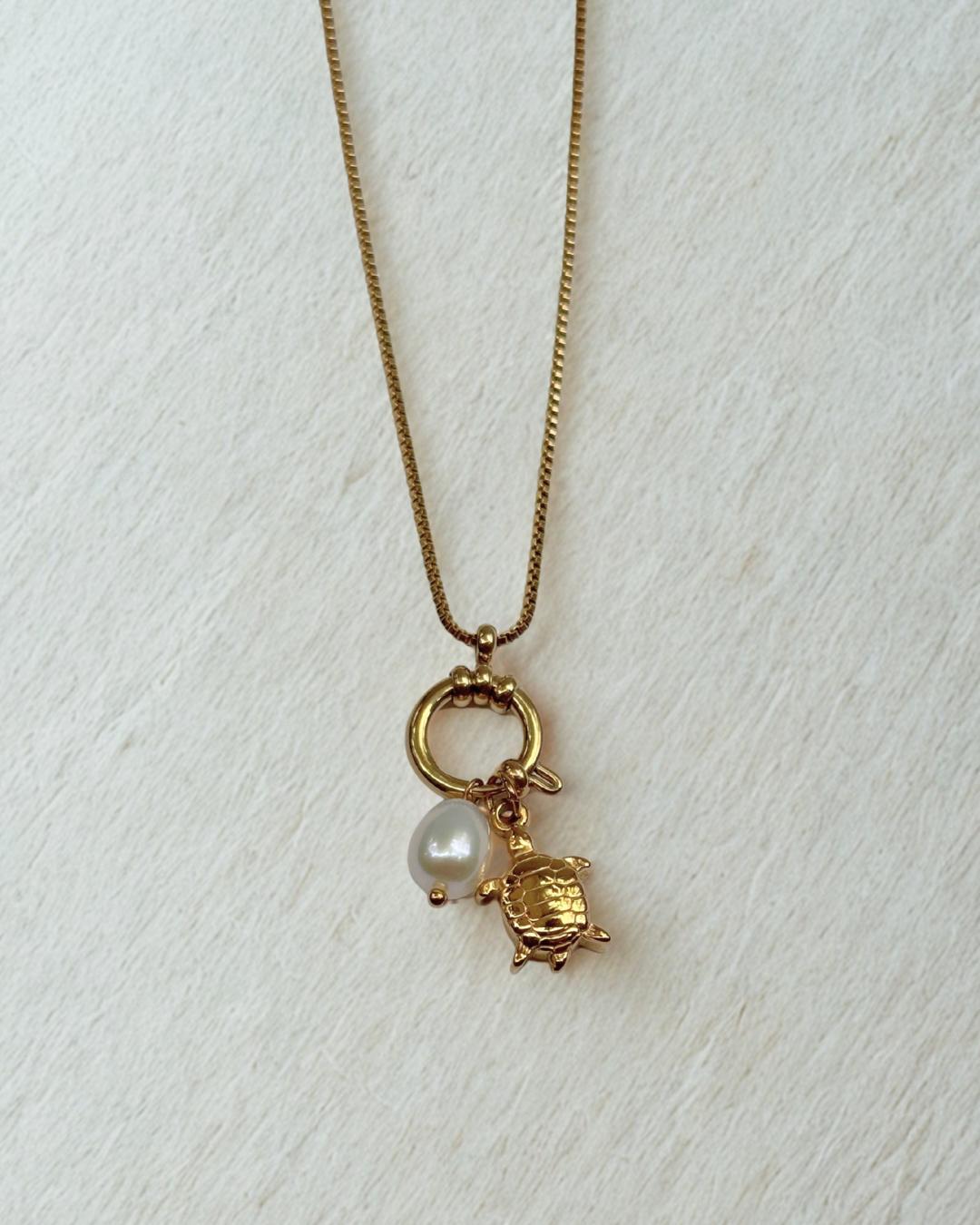 Gold necklace with a turtle and pearl charm on a white background