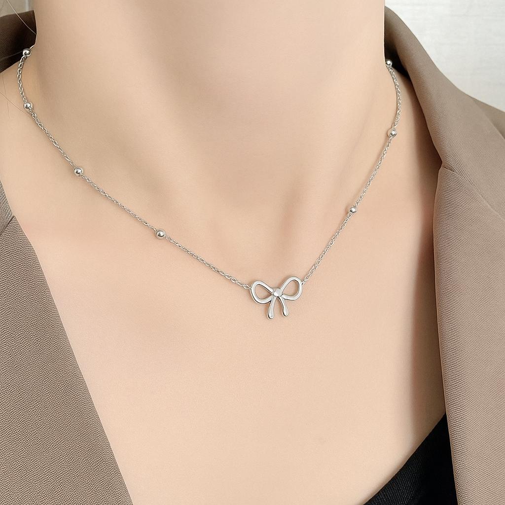 Silver bow-shaped necklace on a person wearing a beige top.