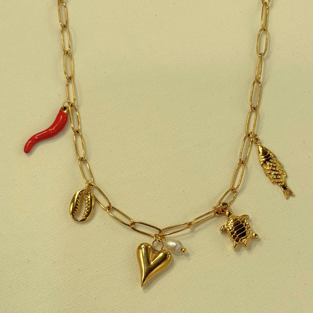 Gold necklace with various charms including a red chili, fish, turtle, and heart on a beige background.
