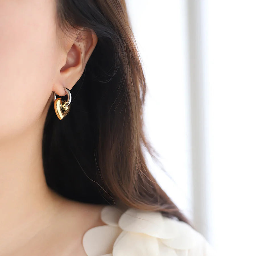 Gold heart-shaped earring worn by a person with a blurred background