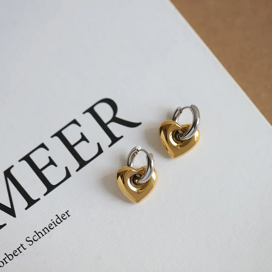 Heart-shaped earrings in gold and silver on a white surface with text.