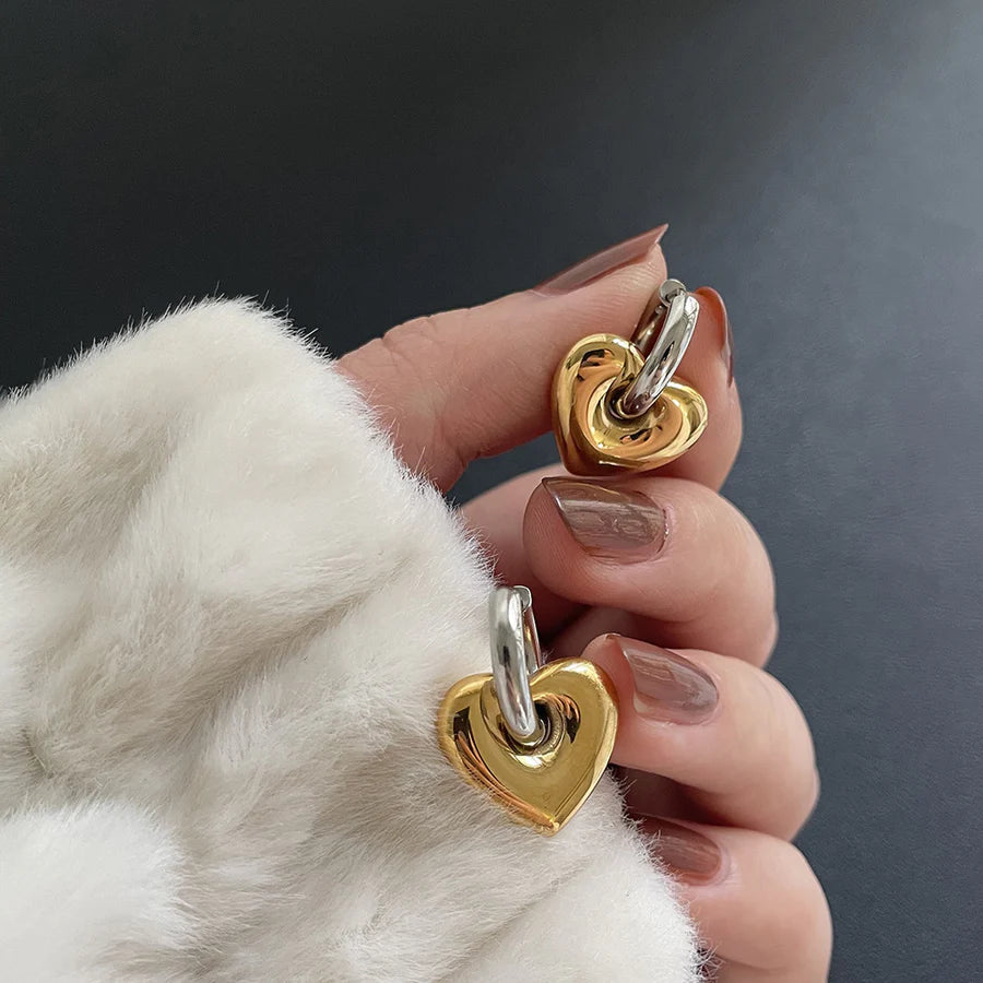 Gold and silver heart-shaped earrings held by a hand with a white fur sleeve.