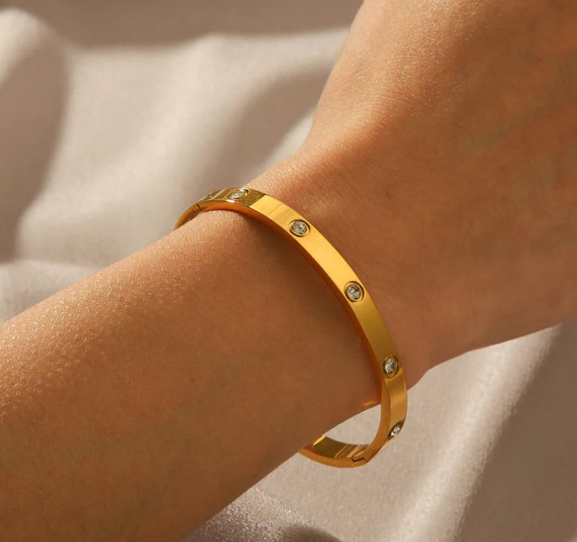 Gold bracelet with embedded stones on a wrist against a neutral background