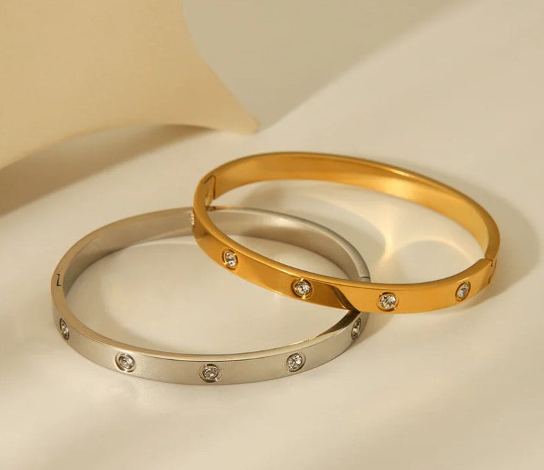 Two gold bangles with embedded stones on a beige background