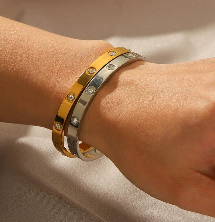 Two gold bracelets with diamond accents on a wrist against a neutral background