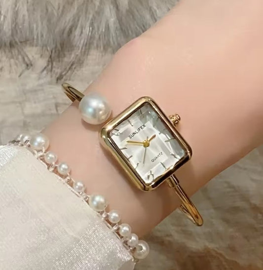 Gold watch with pearl bracelet on a wrist against a neutral background